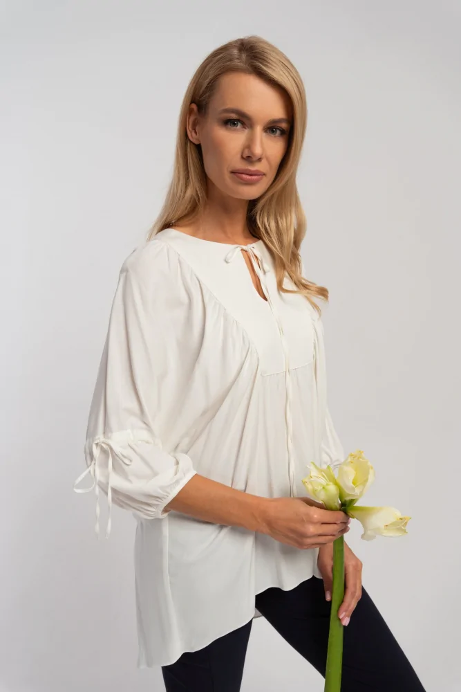 Biała długa bluzka o luźnym kroju z marszczeniami i dekoltem wiązanym na sznurek, z szerokimi długimi rękawami.